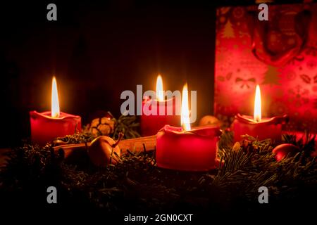 Dekorierter Adventskranz aus Tannenzweigen mit brennenden roten Kerzen vor schwarzem Hintergrund Stockfoto