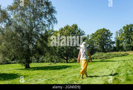 Frau mit langem Zitronenrock und Sonnenhut zu Fuß in Cuckfield in der Nähe von Haywards Heath, Sussex, England, Großbritannien Stockfoto