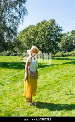 Frau mit langem Zitronenrock und Sonnenhut zu Fuß in Cuckfield in der Nähe von Haywards Heath, Sussex, England, Großbritannien Stockfoto