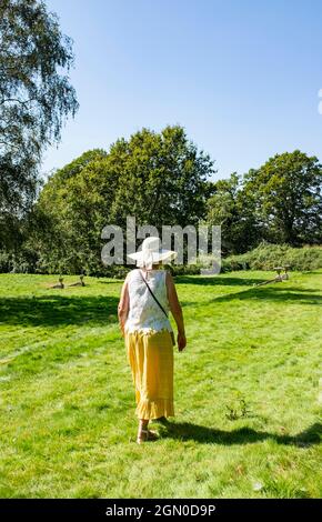 Frau mit langem Zitronenrock und Sonnenhut zu Fuß in Cuckfield in der Nähe von Haywards Heath, Sussex, England, Großbritannien Stockfoto