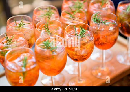 Gekühlte alkoholische Cocktails, die auf den Felsen serviert werden, mit Rosmaringarnitur, die in eleganten Gläsern in Reihen auf einem Buffettisch bei einer Cateringveranstaltung gezeigt wird Stockfoto