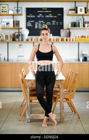 Ruhig lächelnde Frau in Sportswear, die barfuß am Tisch steht und sich vor dem Training im Fitnessstudio entspannt Stockfoto
