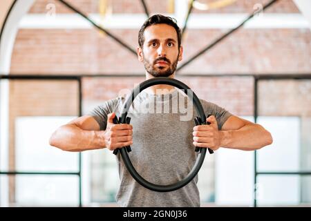 Passen Sie den athletischen Mann mit einem Pilates Magic Circle oder Ring an, um seine Muskeln zu stärken und seine Haltung in einem Fitnessstudio in einer Nahaufnahme des Oberkörpers auszurichten Stockfoto