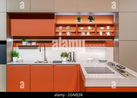 Moderne Einrichtung von Küchengeräten und Schränken in minimalistischem Stil in orangefarbener Farbe Stockfoto