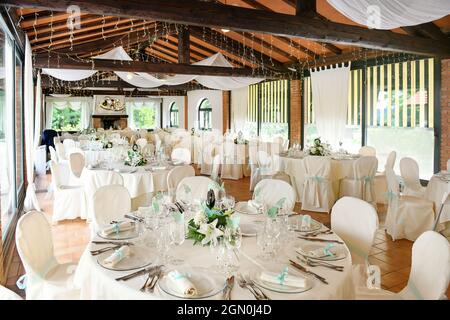 Elegantes Innendesign des Restaurants mit runden Tischen mit Geschirr und Blumen in zarten Weiß- und Blautönen, serviert für festliche Hochzeitsempfänge Stockfoto