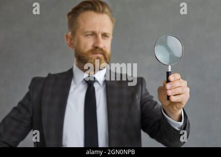 Ein ernsthafter Geschäftsmann, der nach etwas sucht und durch eine Lupe schaut Stockfoto