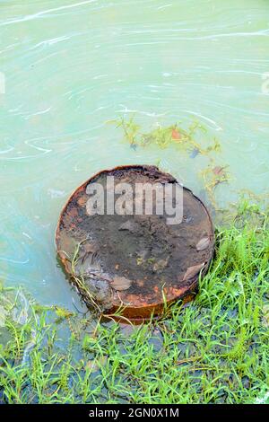 Das Reservoir ist stark verschmutzt, da das alte verrostete Fass Erdölprodukte, einen Ölfilm auf der Oberfläche, abgibt Stockfoto