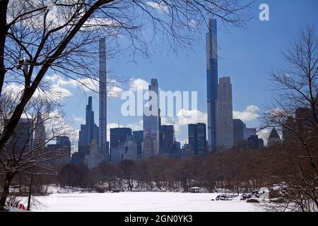 Die hohen Wolkenkratzer des Milliardärs Reihen sich hinter dem verschneiten See des Central Park in New York City Stockfoto