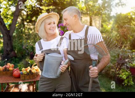 Aktives Seniorenpaar hält Gartengeräte und arbeitet an sonnigen Tagen in ihrem Garten zusammen Stockfoto