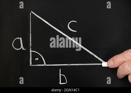 Ein Lehrer schreibt die Pythagoräische Theoremgleichung auf einer schwarzen Tafel, während er eine Gruppe von Schülern in einem Klassenzimmer unterrichtet. Stockfoto