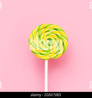 Gelb-grüner Lollipop wirbelt auf einem weißen Stock über rosa Hintergrund. Draufsicht, Platz für Text kopieren Stockfoto