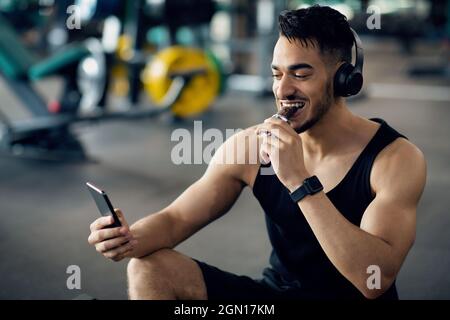 Schöner Muskulöser Arabischer Mann, Der Sich Nach Dem Training Im Fitnessstudio Entspannt Und Protein-Riegel Isst Stockfoto