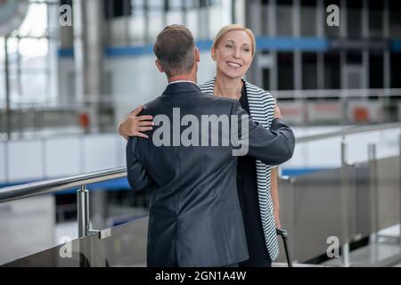 Mann umarmte Frau mit Koffer am Flughafen Stockfoto