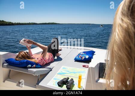 Junge Frau entspannt sich auf dem Sonnendeck eines Le Boat Horizon Hausbootes und liest ein Buch, Lower Rideau Lake, Ontario, Kanada, Nordamerika Stockfoto