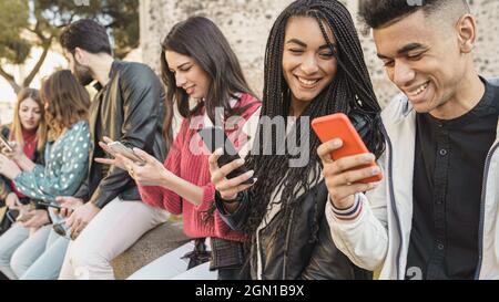 Eine Gruppe von Freunden, die mit ihren Smartphones im Freien spielen – fröhliche junge Menschen, die im Freien mit dem Handy telefonieren. Technisches Konzept. Stockfoto