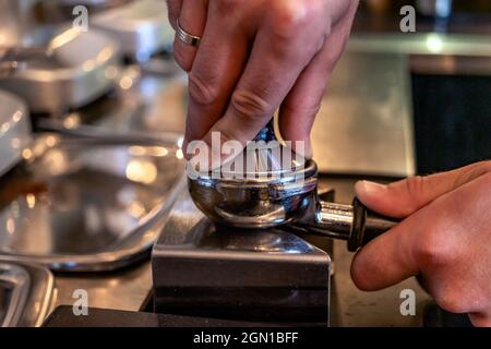 Barista presst gemahlenen Kaffee, um mit einer professionellen Kaffeemaschine eine Tasse Espresso zuzubereiten. Nahaufnahme. Stockfoto