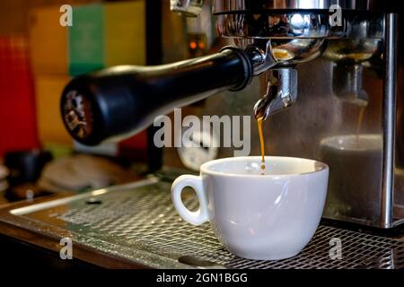 Eine Tasse Espresso mit einer professionellen Kaffeemaschine zubereiten. Nahaufnahme einer weißen Tasse und einem heißen Kaffee aus einer Maschine. Stockfoto