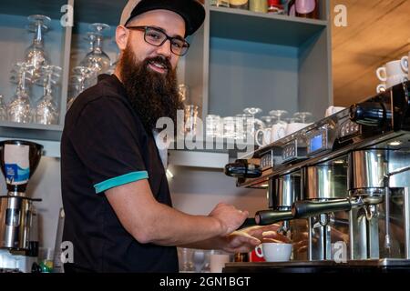 Bärtiger Barista, der mit einer professionellen Kaffeemaschine eine Tasse Espresso zubereitet. Selektiver Fokus. Stockfoto