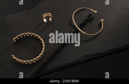 Kettenform und golden mit Diamanten Armbändern und Ring auf dunklen Steinplatten Stockfoto