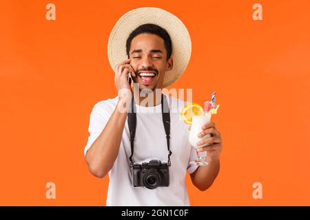 Gerne lustig und charismatisch, aufgeregt afrikanisch-amerikanischer Mann im Sommer Hut, Kamera hängen an Hals und lachte, als Sprechen auf dem Smartphone, jemand anrufen Stockfoto