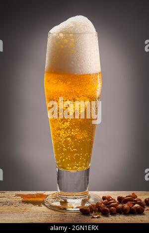 Ein Studiofoto von einem Glas Bier auf einem Holzbrett und ein paar Erdnüsse daneben. Stockfoto