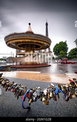 Karussell vor dem Eiffelturm bei Regenwetter; im Vordergrund sind Liebesschlösser an der Kette des Straßenbluffens befestigt; Paris; Île-de-fran Stockfoto