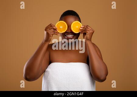 Plus Größe schwarze Frau, die die Augen mit Hälften von Orange bedeckt Stockfoto