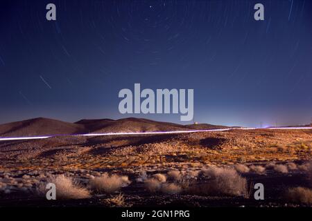 Nachtansicht von Pflanzen und Hügeln in der Wüste mit Licht- und Sternspuren und Nordstern am Rahmen im iran Stockfoto