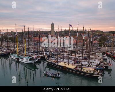 Luftaufnahme von historischen Flachbodenseglern im Hafen von West Terschelling mit Stadt und Brandaris Leuchtturm bei Sonnenuntergang, West Terschelling, Stockfoto