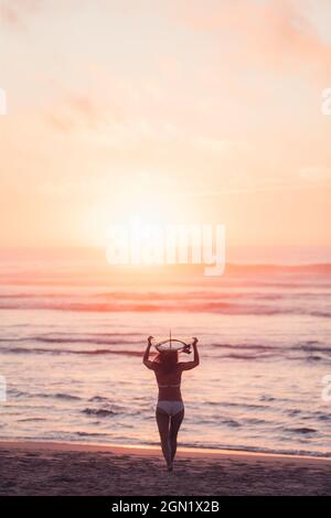 Weibliche Surferin geht mit Surfbrett am Strand in Sonnenuntergang, Surfen, Portugal, Sonnenuntergang Stockfoto