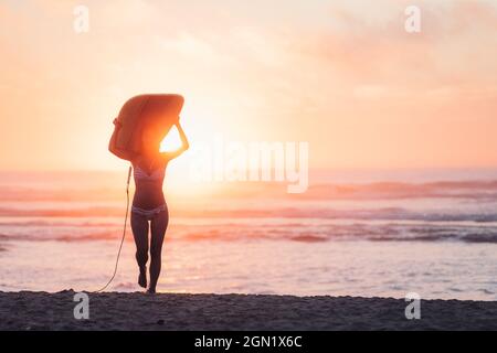 Weibliche Surferin geht mit Surfbrett am Strand in Sonnenuntergang, Surfen, Portugal, Sonnenuntergang Stockfoto