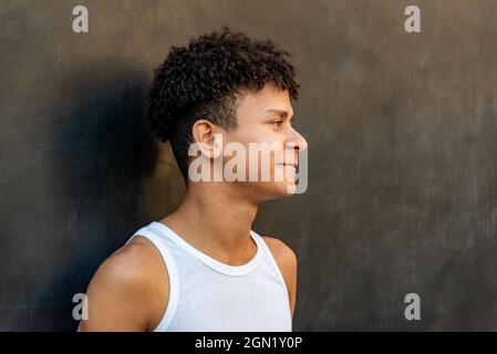 Afro-lateinischer Teenager, der vor einer schwarzen Wand lächelt Stockfoto