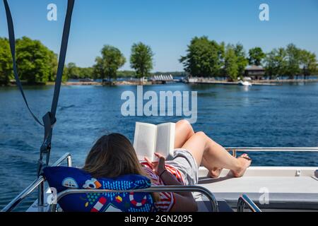 Junge Frau entspannt sich auf dem Sonnendeck eines Le Boat Horizon Hausbootes und liest ein Buch, Big Rideau Lake, Ontario, Kanada, Nordamerika Stockfoto