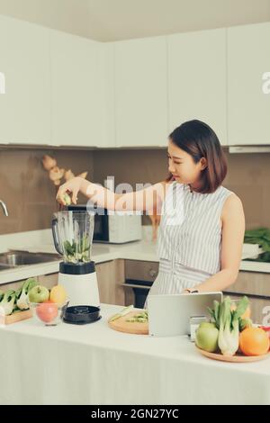 Schöne asiatische Frau entsaften, grüner Saft mit Saft Maschine in der Küche zu Hause. Gesundes Konzept. Stockfoto