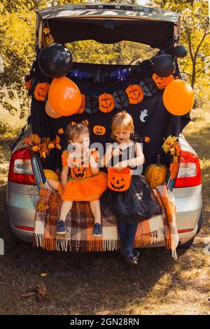 Kinder feiern Halloween im Kofferraum des Autos. Freunde Kinder Mädchen Vorbereitung für Oktober Urlaub im Freien. Trick or Trunk Stockfoto