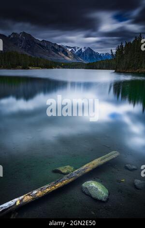 KANADA, ALBERTA, BANFF PARK, LAKE JOHNSON. BLICK AUF LAKE JOHNSON UND DIE KANADISCHEN ROCKIES MIT IM VORDERGRUND SCHWIMMENDEN HOLZTANKERN IM WASSER Stockfoto
