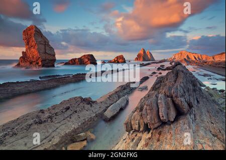 SPANIEN, KANTABRIEN, LIENCROS. BLICK VON UNTEN AUF DEN STRAND VON ARNIA MIT SEINEN GESCHNITTENEN FELSEN BEI SONNENUNTERGANG Stockfoto