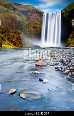 ISLAND, GESAMTANSICHT DES SKOGAFOSS WASSERFALLS IN LANGZEITBELICHTUNG MIT IM VORDERGRUND DER FLUSS Stockfoto