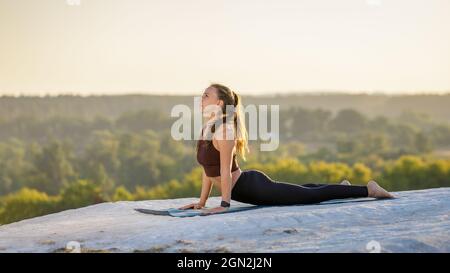 Junge Fitness-Frau, die bei Sonnenuntergang Yoga im Freien macht. Stockfoto