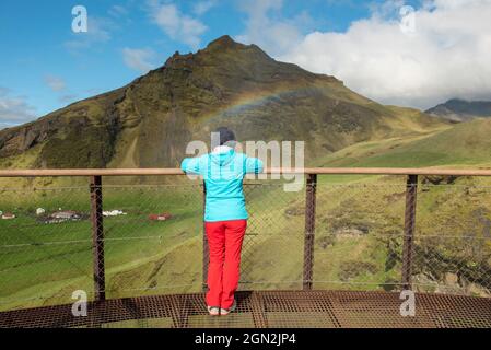 Frau auf der Suche nach ein Regenbogen über dem Wasserfall Skogafoss in Island Stockfoto