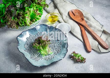 Moderne Keramikschale mit Salatbesteck aus Holz und Salatschüssel auf steinernem Hintergrund Stockfoto