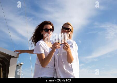 Zwei junge Frauen ruhen sich bei Sonnenuntergang auf einer Yacht im offenen Meer aus. Stockfoto