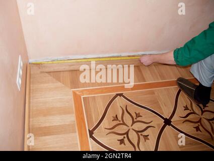 Montage und Reparatur von Holzstäben auf Eichenparkett. Auftragnehmer Hände messen Holzschlagstock mit Maß Hahn. Stockfoto