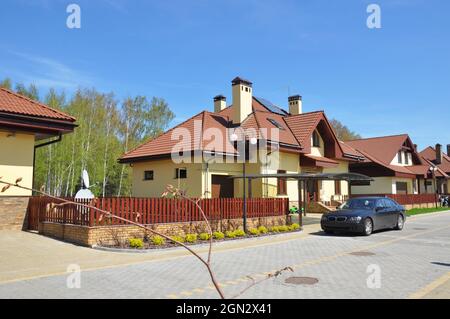 Modernes Haus mit Sonnenkollektoren, Oberlichtern, Garage und Neuwagen auf der Straße der Vorstadthäuser im frühen Frühjahr Stockfoto