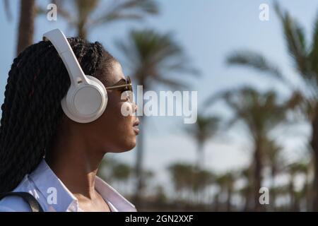 Junge Frau hört Musik mit kabellosen Kopfhörern, während sie im Freien steht Stockfoto