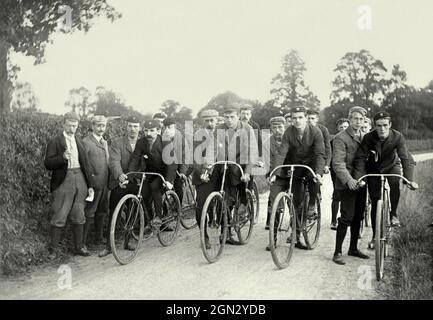 Radfahren in Großbritannien im viktorianischen Zeitalter. Hier ist eine Gruppe von Fahrern kurz vor dem Start zu einem Rennen oder Zeitfahren auf ländlichen Nebenstraßen um 1900. Der Starter ist links, und andere Beamte unterstützen jeden der acht Teilnehmer. Die Radfahrer tragen überraschend modern aussehende Ausrüstung mit Rundhalsausschnitt-Sweatshirts oder T-Shirts und weichen Lederschuhen, die Ähnlichkeiten mit den heutigen leichten Turnschuhen haben. Jeder trägt eine Mütze. Dies ist aus einem kleinen Bild in einem alten Fotoalbum – einem Vintage-Sportfoto – entnommen. Stockfoto