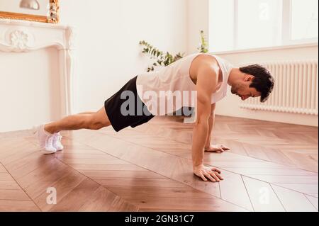 Schöner muskulöser Mann in einem T-Shirt und Shorts, der zu Hause am Boden Funktionsübungen macht Stockfoto