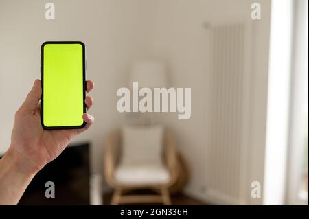 Mockup Bild der Hand hält schwarzes Handy mit leerem grünen Bildschirm und Hintergrund moderne Innenausstattung Stockfoto