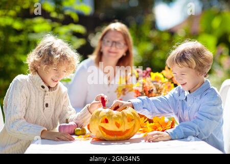 Familie Schnitzerei Kürbis für Halloween-Feier. Eltern und Kinder schneiden Jack o Laterne für traditionelle Trick or Treat Dekoration im sonnigen Garten. Stockfoto