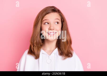 Foto von süßen charmanten kleinen Schulmädchen gekleidet weißen Sweatshirt lächelnd suchen leeren Raum isoliert rosa Farbe Hintergrund Stockfoto